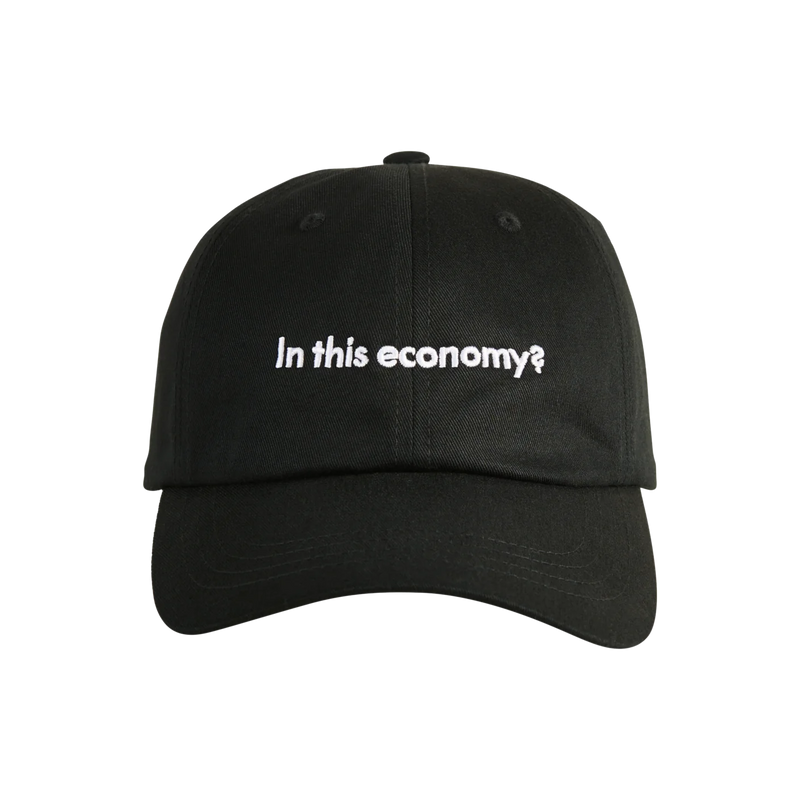 A black, curved-brim hat with the words “In this economy?” written on its crown.