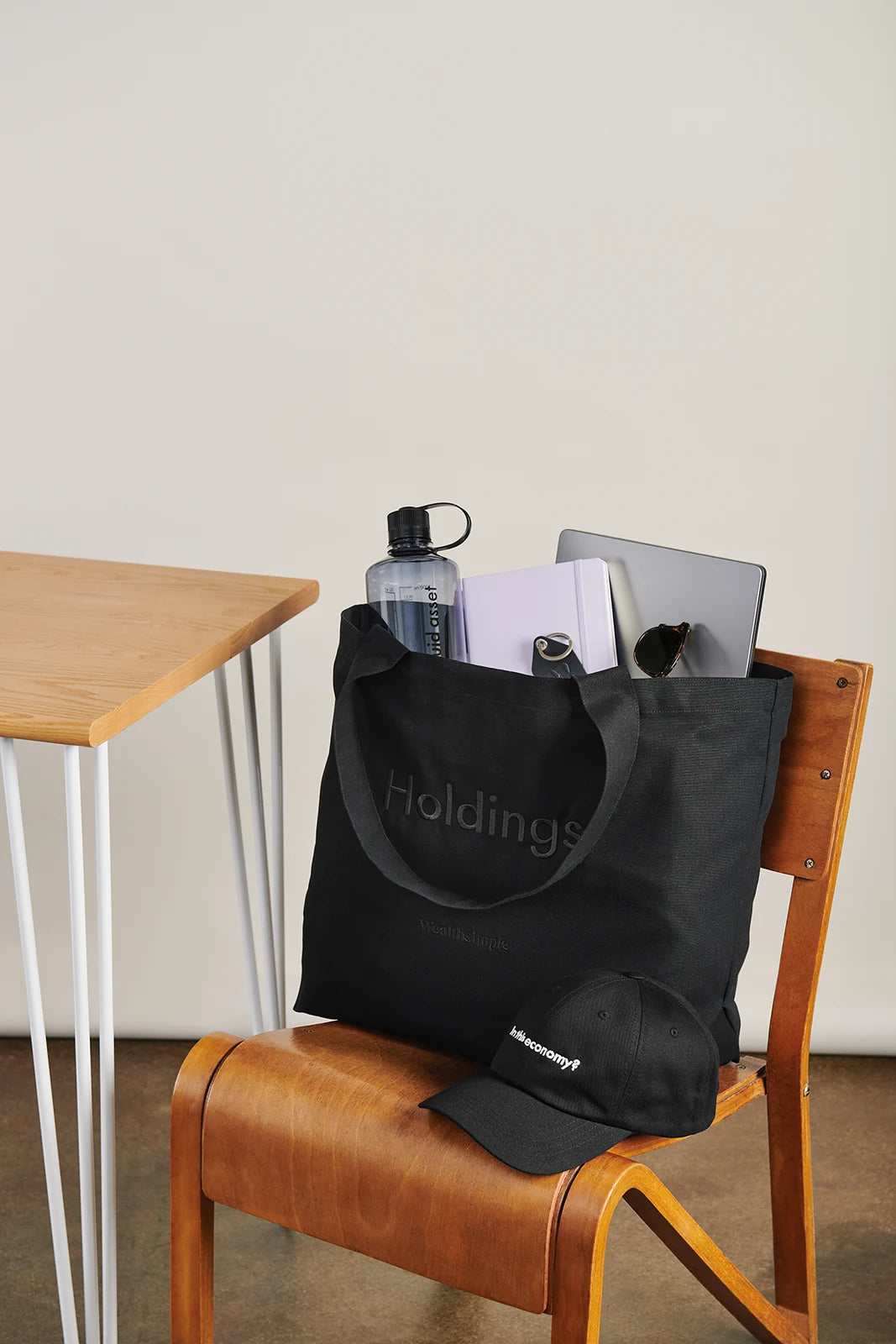 A Wealthsimple tote bag placed on a green chair. It&rsquo;s filled with a branded water bottle, a cap, and a laptop.